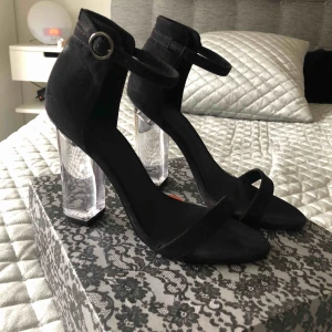  - Snygga klackar från Nelly. Svart mockaimitation, glasklar klack och spänne vid ankeln. Klackhöjd 10 cm. Endast använda vid 2 tillfällen, så sparsamt använda! 