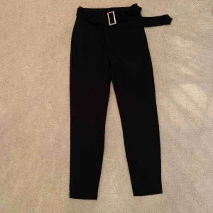  - Ett par svarta kostymbyxor med ett stretchigt material, i midjan är det ett skärp man kan ta bort å dem har fickor fram  alldrig använda 
