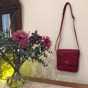  - Vinröd liten väska med magnetknapp och flera små fack för förvaring. Den är knappt använd. Längden på axelbandet går att justera. Materialet är veganskt. Texturen och mönstret är superfint🌷🌻🍃