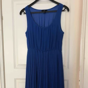  - Blå klänning med plisserad kjol och elastisk midja. Klänningen är kortare framtill. Använd endast ett par gånger och är i nyskick. Hämtas i Malmö eller skickas mot frakt. 