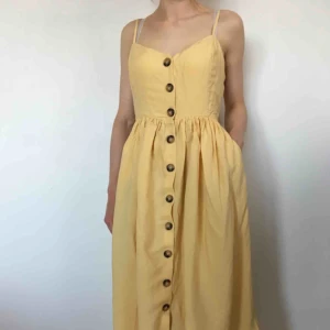  - Gul klänning i strl 36. Knappar framtill och fickor på sidorna i kjolen. Justerbara axelband.