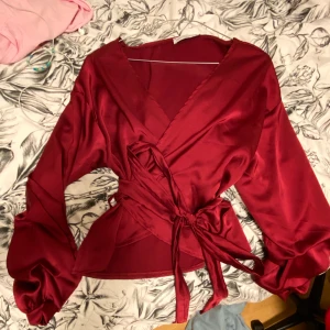 Satin tröja från Bohoo - Snygg vinröd satin-omlott-tröja i storlek S från Bohoo. ALDRIG använd eftersom jag inte kände att det var min stil när jg fick hem den :( Armarna he någon refflad detalj längst ner vid armen. köparen står för frakten om inte mötas upp i Stockholm.