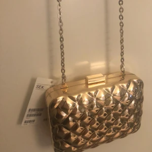  - Jättefin väska i färgen guld, i hårt material. Fick i present med aldrig använd (prislapp kvar) Nypris 399/499. Just nu på rea för 70kr 