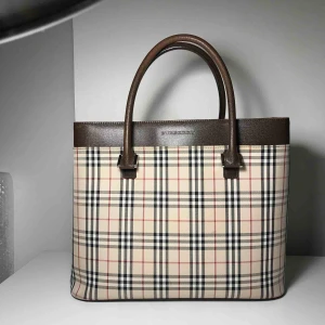  -   Burberry väska Mått 34x 28x 12 Ingen kvitto Väskan är fint begagnad skick, med rymlig med 2 stycken små fack och ytterfack samt ett fack i mitten, finns en liten slitage.  Pris: 3100kr  
