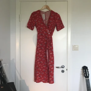  - Klänning i samma print som det franska märket Rouje, i tunt tyg med omlott och knappar vid midjan. Nyss inköpt men säljes pga fel storlek. Köparen betalar frakt.
