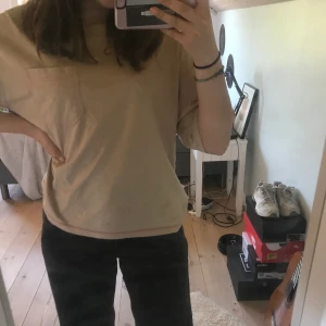 Beige/rosa t-shirt - En beige t-shirt med rosa sömmar. En ficka. Använd få gånger. Passar dig med storleken sx/s. OBS: har råkat spilla tre små klorinfläckar längst ned i kanten, syns inte mycket men brukar stoppa in den i fram😊 