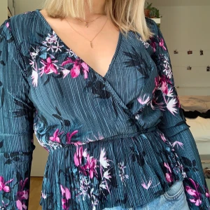 Blommig omlottblus från Gina, stl XS - Blusen köptes från Gina Tricot för ca 2 år sen, dock endast använd en gång. Storlek är XS, men bandet i midjan är strechigt vilket även tyget är till viss del. Mycket bra skick! Frakt ingår ej.
