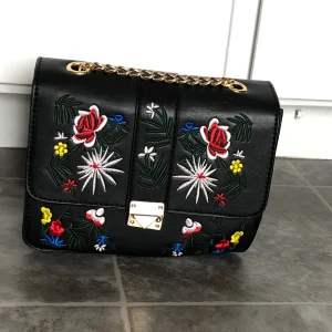 blommig väska - en gullig väska med broderade blommor och guldkedja:) har en liten ficka där i ock är endast använd ett fåtal gånger! passar perfekt till en mer basic outfit 🥰