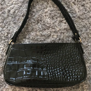Svart väska i ormskinn - Fin svart liten väska i ormskinnsliknande material. Helt oanvänd så därmed i väldigt fint skick