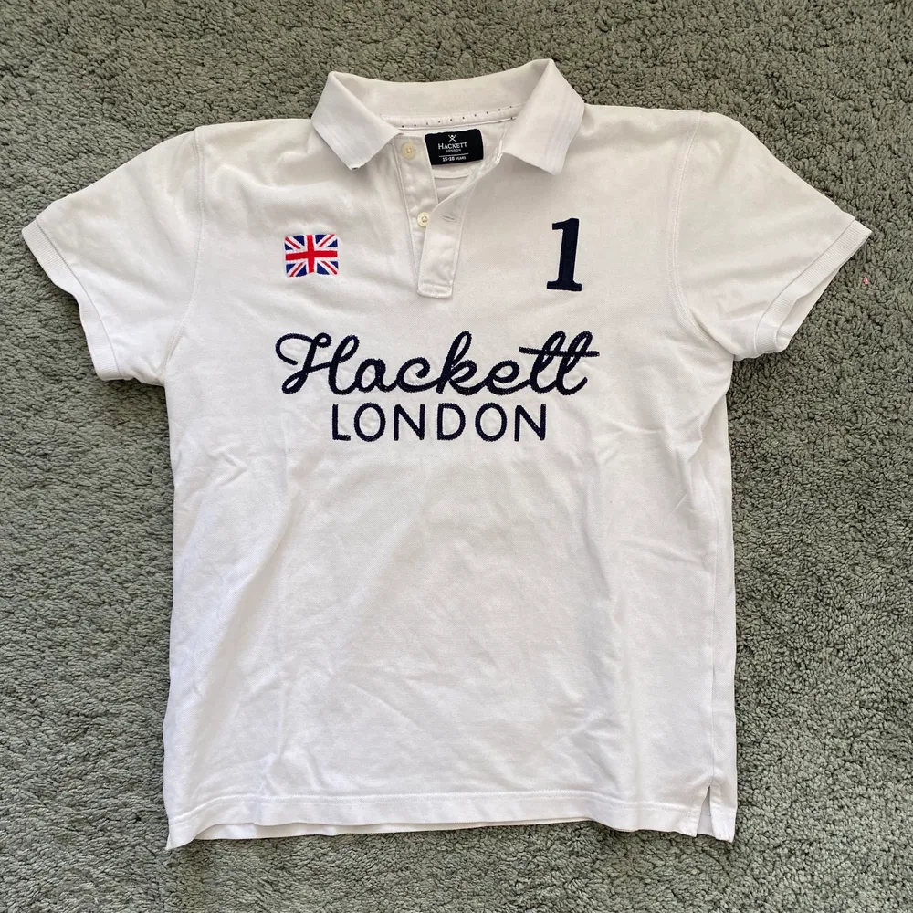 En vit Hackett piké med en stor ”1” på ryggen, utmärkt skick. Storlek 15-16 år. T-shirts.