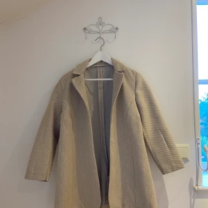 Beige kappa - Beige kappa köpt på Emmaus Secondhandstore. Aldrig använd. Lite hårdare material. Sömmarna syns på insidan men inte när man bär kappn. 