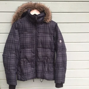  - Kort och sportig dunjacka från Columbia i rutig mörkgrå mönster. Storlek S och är true to size. 60%  dun och 40% fjäder. Mycket fint skick, inte nopprig, inga fläckar och andra användningsspår. Kapuschongen kan tas av. Två fickor med dragsko och en liten innerficka. Fuskpäls som sitter fast vid kapuschongen. Frakten tillkommmer: 65kr med Skicka lätt. Eller mötes upp i Stockholm.