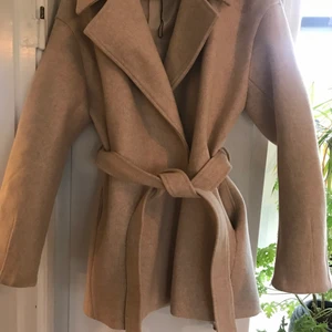 Beige kappa NAKD strl 36 - Fin beige kappa/jacka med knyt i midjan samt en tryckknapp framtill. Storlek 36 inköpt i januari iår men endast använd 1 ggr. Passar en 36/38:à frakt på 95kr tillkommer 