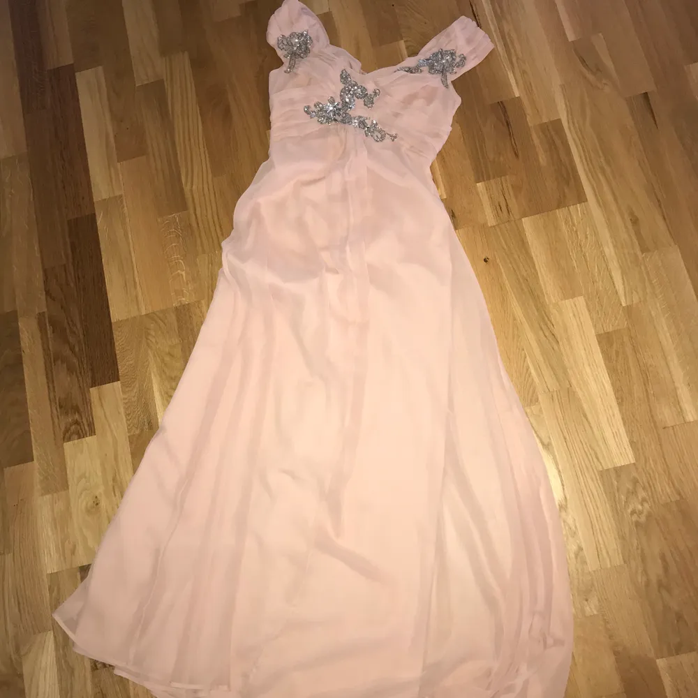 Denna klänning kan användas till bal eller bröllop ex.  Den har en ljus gammelrosa färg med silvriga stenar, paljetter som detalj på överdelen. Klänningar.