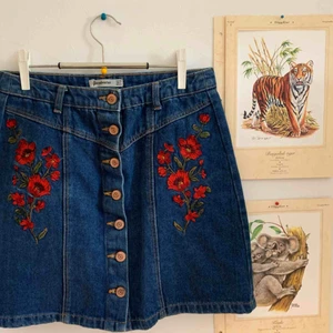  - supersöt jeanskjol från stradivarius. använd fåtal gånger. fina broderade vallmoblommor på både höger o vänstersida om knapparna🧡 köparen står för frakten.