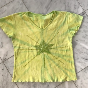 Gullig topp - Tie-dye tshirt i mycket gott skick. Endast använd ett fåtal gånger. Passar för de flesta storlekarna, beror på vilken passform man vill ha. Klädmärket är okänt. Motiv i mitten av tröjan av en stjärna gjord av paljetter och pärlor. 