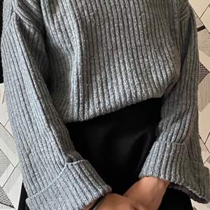 En grå stickat tröja som är perfekt inför vintern. Den är rullad i nacken och uppvikt vid armen 