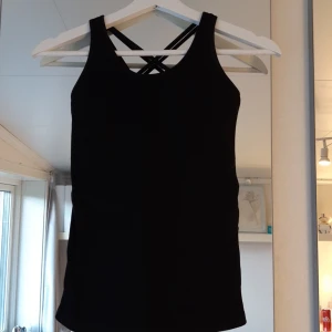 Träningslinne - Ett svart träningslinne i storlek XS. Bekvämt och med snygga detaljer med snören på ryggen. Inbyggd sporttopp och använd några få gånger.