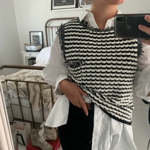 Trendig stickad väst - Trendig stickad väst i svart och vitt mönster med fransdetaljer och snygga knappar i bak, aldrig använd, stl S, snygg att ha som den är eller med en skjorta som jag har på bilden eller någon annan långärmad tröja, funkar även över en klänning!