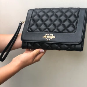 Love Moschino clutch - Äkta Love Moschino väska i nyskick, svart clutch med handrem. Pris 200kr + frakt. Säljs pga används aldrig.