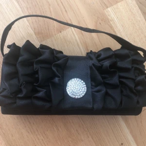  - Supersöt liten ”clutch/kuvertväska” i svart silkesmaterial och kristallamulett. Magnetlås. Använd endast en gång. Mötes upp i T-Centralen eller Skogås, fraktar mot kostnad  