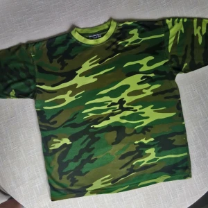  - Camouflagemönstrad T-shirt i strlk L. Inköpt på Humana för 150kr. Det finns ett pyttelitet hål på framsidan av tröjan, se bild nr 3. Köparen står för frakt. 