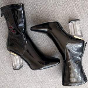 Svarta boots i glansigt lack/PVC fuskläder. Med dragkedja och perspex klack. Klackhöjd ca 5 cm, fyrkantig tå. Supertrendiga! Endast använda en gång inomhus. De passar en vanlig storlek 37. Hämtas/möts upp i Stockholm för köp eller 49 kr frakt. 