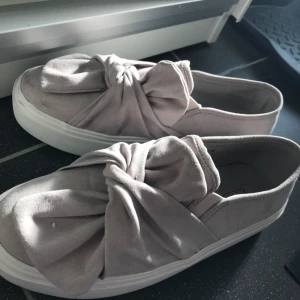  - Ett par grå skor från Nelly med rosett vid framsidan i storlek 38, passar även strl 39. Helt nya, har aldrig använts. Säljer för 180kr!