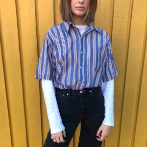  - En t-shirt skjorta med blåa, röda, vita och orangea ränder. Jättefin att ha både stängt och öppen med en tröja under🥰