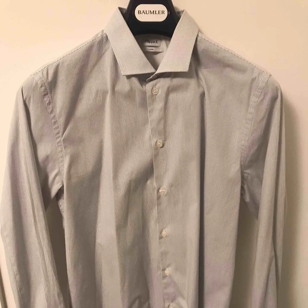 Snygg vit skjorta med gråa ränder från Filippa K. Sällan använd som mest hängt i garderoben då jag snabbt växte ur den. Storleken är Large. Kan fraktas mot avgift.. Skjortor.