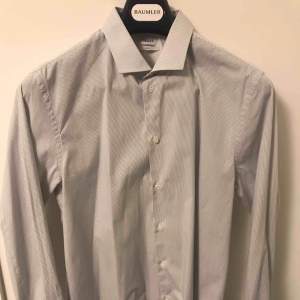 Snygg vit skjorta med gråa ränder från Filippa K. Sällan använd som mest hängt i garderoben då jag snabbt växte ur den. Storleken är Large. Kan fraktas mot avgift.