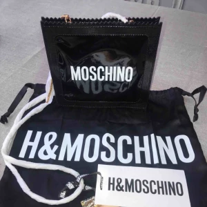  - BUD PÅ TRADERA! En helt oanvänd MOSCHINO [TV] H&M axelremsväska. Den är i en lackad läderimitation med textryck fram och bak och med en guldpläterad ormlänk - Dustbag ingår och allt annat som kom med.-Jag tar inte ansvar för postnords hantering