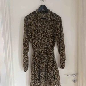 - Klänning i leopardmönster från Bikbok. Snöre i midjan och knappar. Svart underklänning.   Ny och aldrig använd. Passar från xs-m
