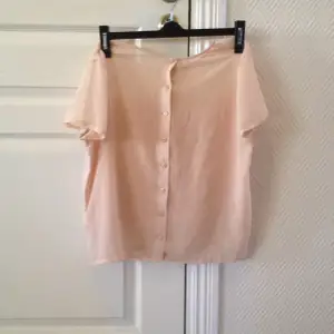 Pastellrosa t-shirt med tunnt tyg och knappar i ryggen. 