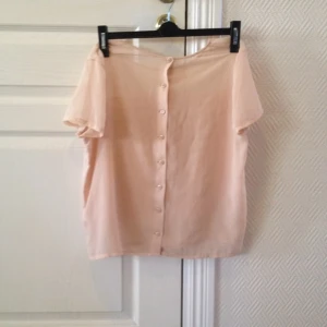 Pastellrosa t-shirt med tunnt tyg och knappar i ryggen.  - Pastellrosa t-shirt med tunnt tyg och knappar i ryggen. 