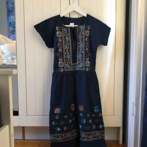  - Vintage!  Marinblå klänning med markerad midja och vackra broderier framtill, enfärgad rygg. Dragkedja i sidan och litet knäppe fram. Upphämtas i centrala Uppsala. Porto tillkommer vid frakt, 54kr
