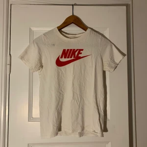Nike t-shirt  - Vit Nike T-shirt med röd logga/swoosh i jätteskönt material. Strl XS. (Obs! Ser ur som en fläck vid bröstet på bilden men är som ett litet hål/tyget har blivit slitet där men syns ej när man har den på sig) 
