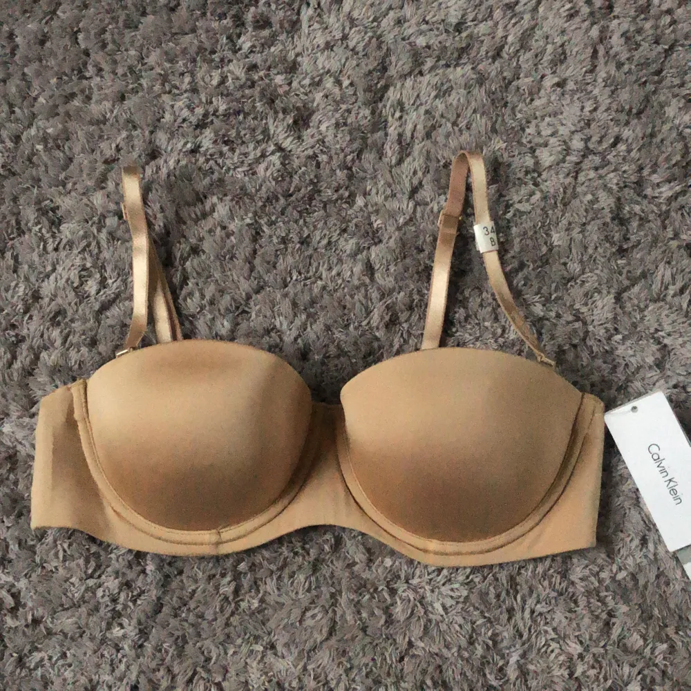 Den perfekta balconette/strapless bh från Calvin klein i hudfärg. Den är super skön och sitter uppe men är tyvärr för liten. Den har pushup band som är avtagbara. Det sitter ”plast” vid sidorna så att den ska sitta uppe. Storlek 34b/75b. Köpt för 500kr💞. Övrigt.