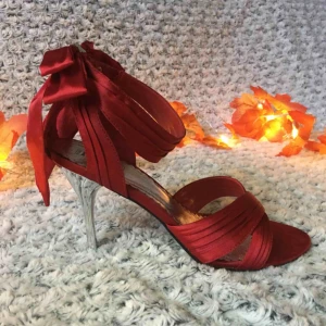  - Röda sandaletter / pumps i satin, med söt rosett baktill och snygg silverfärgad klack. Endast använda ett fåtal gånger, sula och klack i perfekt skick. Stl.40