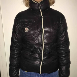  - Moncler jacka i storlek S, svart och med avtagbar huva. Ingen dragkedja men knappar. Ett litet hål i högra armvecket inne i jackan. Går lätt att sy igen. 