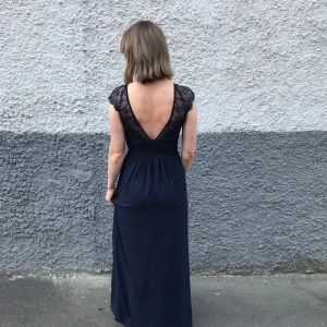 Festklänning  - Hellång mörkblå klänning med djupt uringad rygg och spettsprydda axlar. Inköpt på ASOS. Använd ett fåttal gånger och i gott skick. Storlek 38. Jag som bär klänningen på bilden är 170 cm lång och har vanligtvis storlek 36-38. 