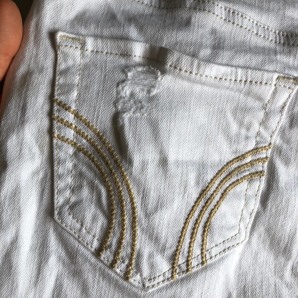 En kort, vit och tight jeanskjol från Hollister. Kjolen är flera år gammal men den har legat längst bak i garderoben bortglömd, inte använd mer än 3 gånger. Snygga detaljer med slitningarna. Köparen står för frakt!. Kjolar.