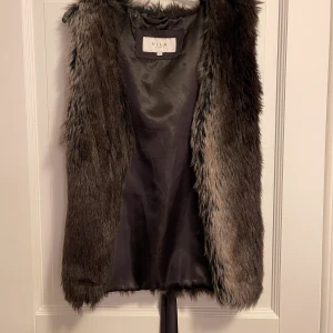Väst i fuskpäls  - Brun väst i fuskpäls, väldigt fint skick. Från Vila i storlek M. 