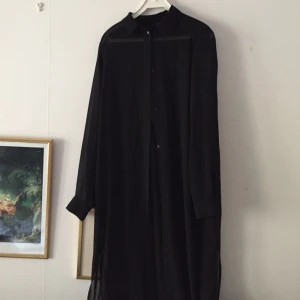  - Lång svart skjorta i tunt tyg. Något genomskinlig och lös passform. Passar en strl.40 med. Jag är 166cm och den når till halva vaden, slits på vardera sida som går upp till övre delen av låret. 

Köparen betalat frakt, kan annars hämtas i Göteborg. 