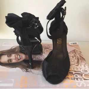  - Sandalett i svart siden med svart sidenrosett på hälen. Elegant och stilfull.   Köparen betalar eventuell frakt