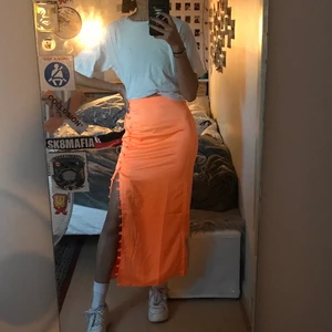 Orange neon kjol med slits- Asos - Orange neonkjol med slits med knäppning från ASOS design. Helt oanvänd med lapp kvar, säljer pågrund av att jag inte orkar skicka tillbaka den utan det vore smidigare att sälja vidare den. Den är helt slutsåld på Asos. Hör av er vid frågor och fler bilder
