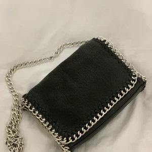 Scorett väska - Säljer denna väska i svart skinnimitation som är köpt från Scorett. Väskan har ett vanligt fack med dragkedja samt ett litet fack dragkedja på baksidan. Modellen heter Pricilla och är från Tiamo. OBS Väskans helhet är okej, färgen på knäppet som stänger väskan är bortslitet, däremot syns det ej utifrån. Förutom det är skicket fint. Köparen står för frakt. 