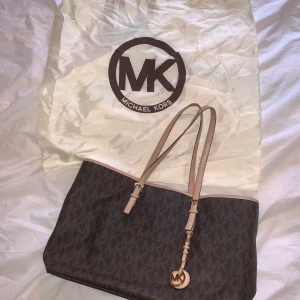 Michael Kors handväska  - Äkta brun och beige handväska från Michael Kors. Lite slitningar på axelremmarna, men annars i mycket fint skick! Rymlig, dator, laddare, A4 papper, etc, får plats. Flera mindre fack, samt fi ja för dator i mitten. Ka  skickas. Köparen står för eventuell frakt. 