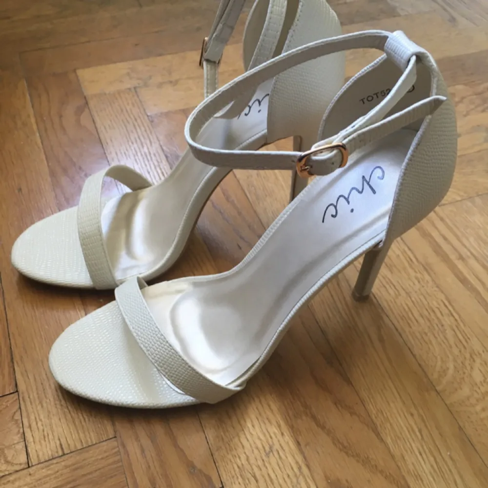 Vita högklackade skor med ankelband. 12 cm klack, i vit skinimitaion med textur. Säljer pågrund av fel storlek. Aldrig använda. Hämtas i Stockholm.. Skor.