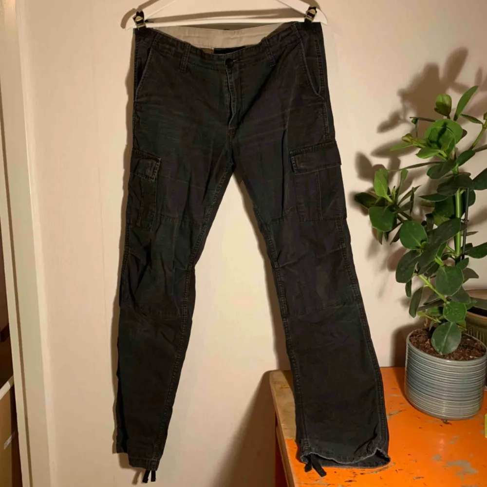Carhartt Cargo Pants, svarta men nu snyggt urtvättade & mer åt de gråa hållet.  Praktiska fickor, justerbar midja & reglerbara i ändarna på benen.  Knappen i midjan är utbytt & den sitter lite löst men är lätt att sy dit ordentligt igen!. Jeans & Byxor.